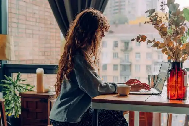 Young woman with curly hair working at the cafe remote office using laptop. Panorama banner. Selective focus.