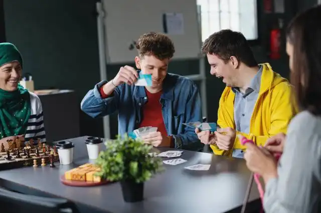 Group of happy people playing cards and board games in community center, inclusivity of disabled person.