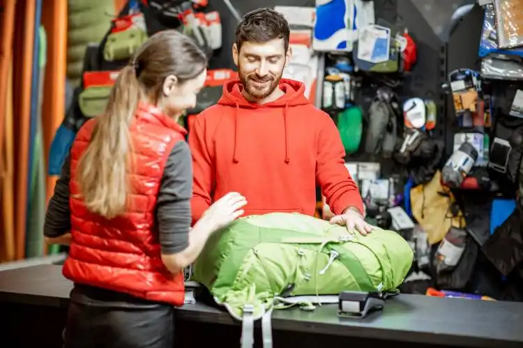 Young woman buying some sports goods standing with salesman at the counter of the shop