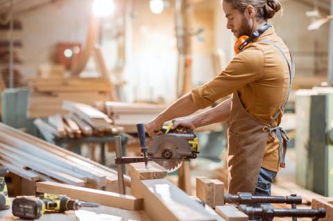 Carpenter sawing wooden bars with cordless electric saw at the joiner&#x27;s workshop