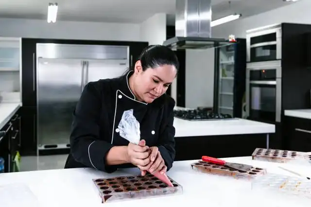 latin woman pastry chef wearing black uniform in process of preparing delicious sweets chocolates at kitchen in Mexico Latin