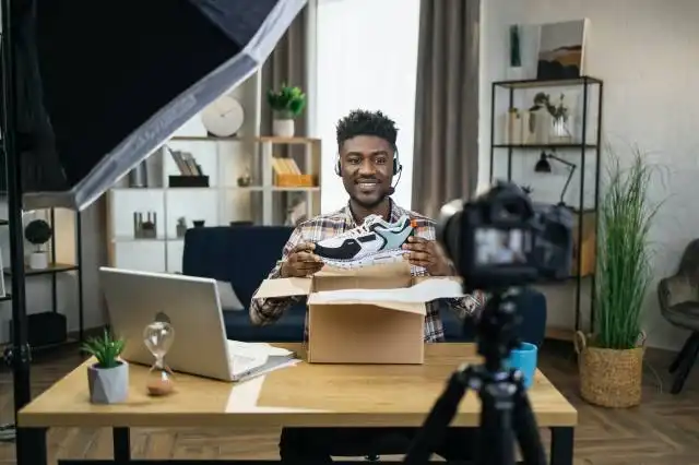 Stylish african man doing unpacking of new sneakers while recording video on camera. Concept of people, blogging and advertis