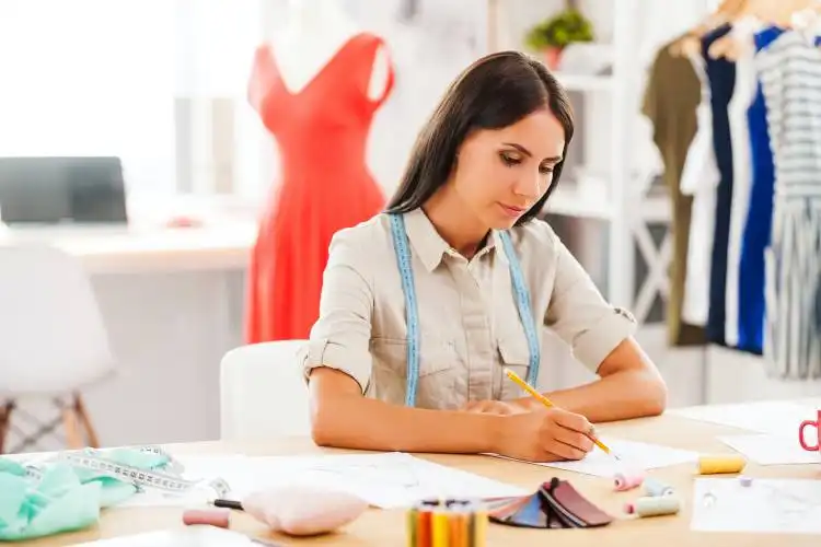 Serious young woman drawing while sitting at her working place in fashion workshop