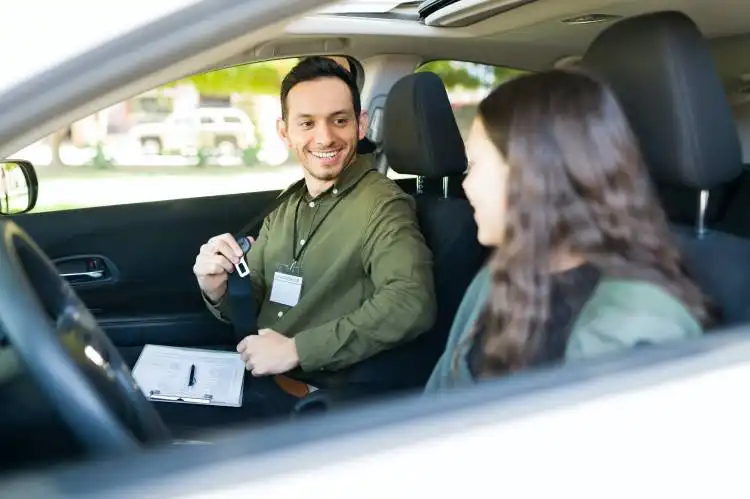 Happy male instructor smiling and teaching a teenage girl student to drive. Adolescent girl feeling nervous during her first