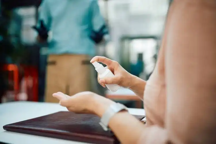 Close-up of woman spraying her hands with disinfectant while being at restaurant,