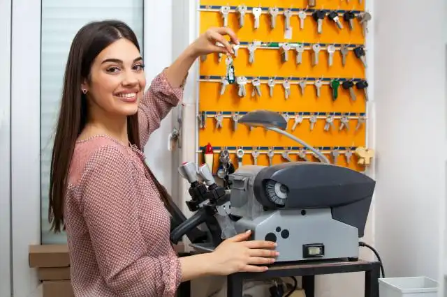 Professional skilled key cutter making door keys copies in locksmith. Young professional with different types of keys in lock