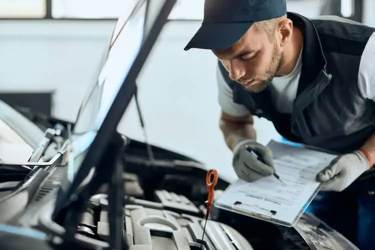 Young mechanic checking car oil and taking notes while working at auto repair shop.