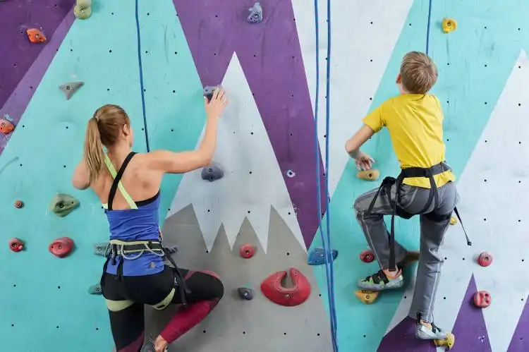 Back view of schoolboy and young woman in activewear grabbing by small rocks on climbing wall during sports training