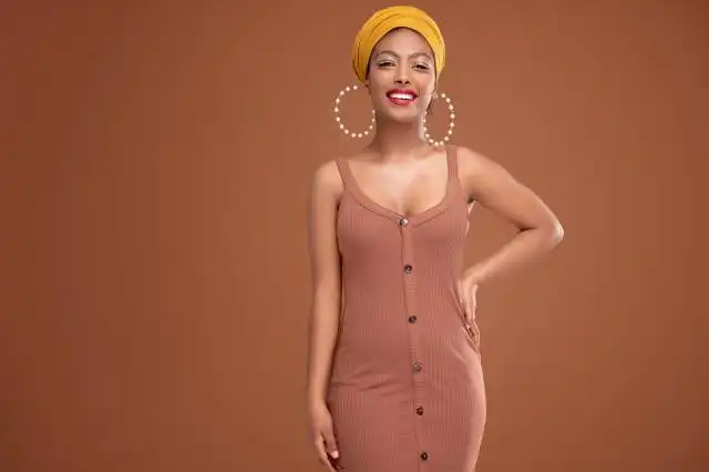 Fashionable beautiful african woman wearing shawl on head and big circle earrings, smiling isolated on brown studio backgrou