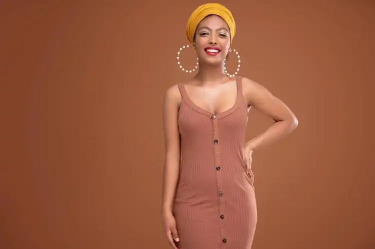 Fashionable beautiful african woman wearing shawl on head and big circle earrings, smiling isolated on brown studio backgrou