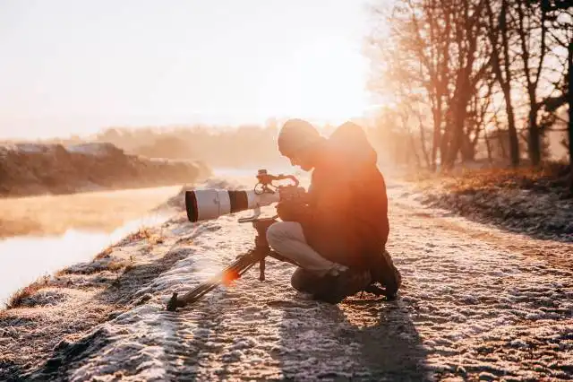 a man kneeling down next to a river with a camera