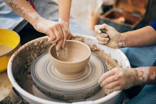 Pottery workshop. Hands of adult and child making pottery, working with wet clay closeup. Process of making bowl from clay on