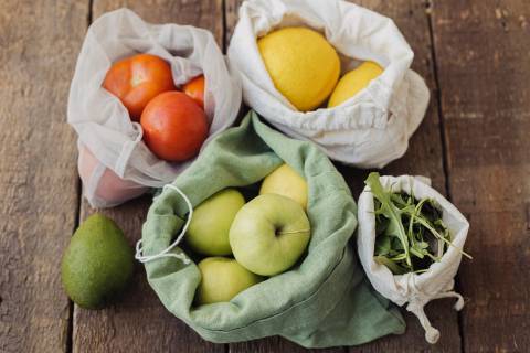 Zero waste shopping. Fresh apples, tomatoes, lemons,avocado and arugula in eco cotton bags on rustic wooden table. Organic fr