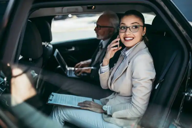 Good looking senior business man and his young woman colleague or coworker sitting on backseat in luxury car. They talking, s