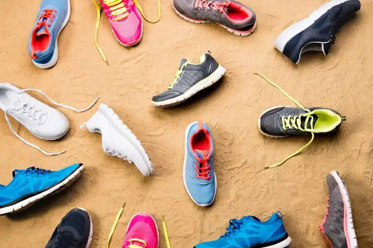 Various colorful sports shoes laid on sand beach background, studio shot, flat lay.