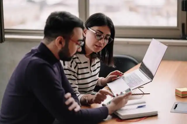 two people sitting at a table looking at a laptop