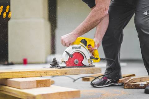 man in black sweatpants using DEWALT circular saw and cutting a wood plank