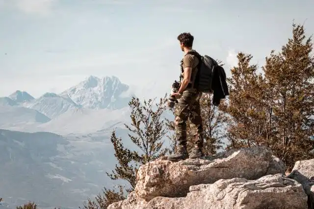 man in black jacket and brown pants sitting on rock formation during daytime