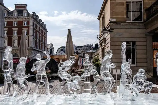 man in white jacket sitting on brown wooden bench near water fountain during daytime