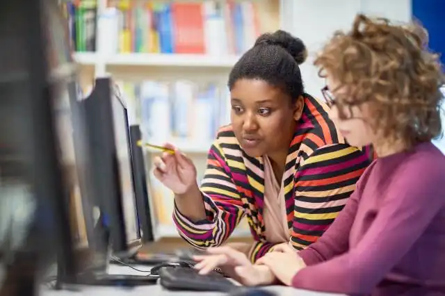 African young teacher pointing at monitor assisting student in using computer at university
