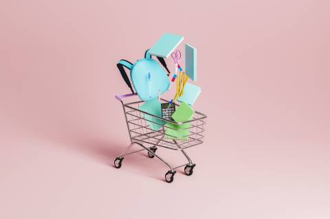shopping cart with school supplies falling inside it with pastel red minimalistic background. concept of education, back to s