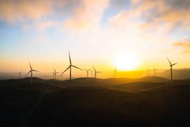 a group of windmills on a hill at sunset